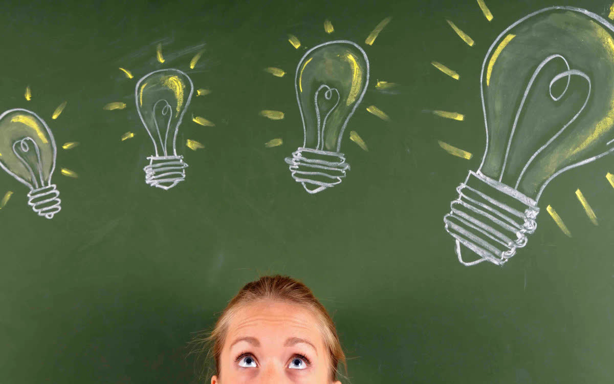 Top 10 Fragen zum privaten Autoverkauf Frau schaut nach oben zu mit Kreide gezeichneten Glühbirnen auf einer grünen Tafel